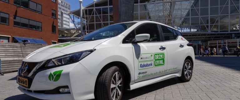 Stockbeeld van een buurauto, een witte elektrische Nissan Pulsar geparkeerd voor een treinstation