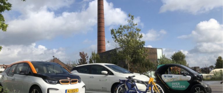 Stockfoto van een vloot van voertuigen die bijdragen aan deelmobiliteit. We zien drie verschillende modellen elektrische auto's. Daartussen prijkt een geelblauwe OV-fiets