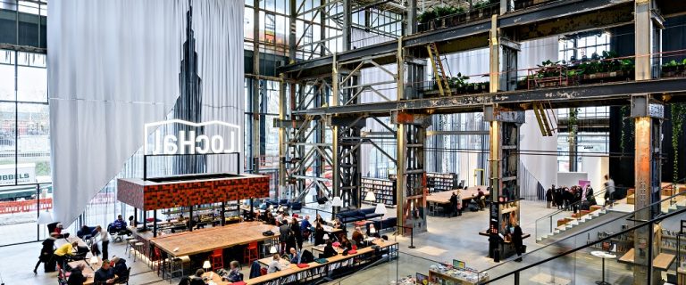 Detailbeeld van het interieur van de LocHal in Tilburg, we zien de trap die tevens als tribune dient en kijken uit op studieplekken in carré-vorm in het midden van de hal