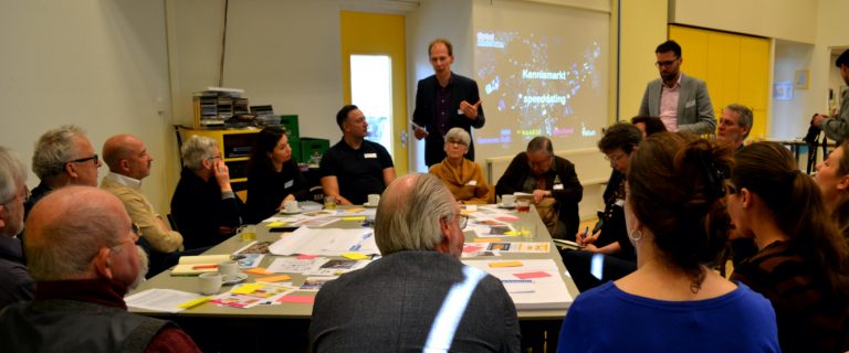 Bewoners en professionals in gesprek aan een grote tafel vol met post-it briefjes tijdens de kennismarkt van het stadslab Vergrijzing op 7 februari