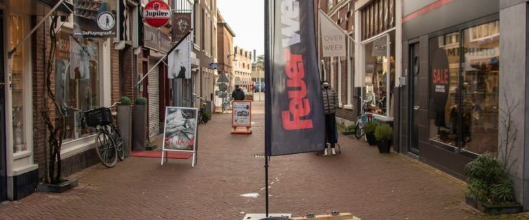 Een bankje dat bestaat uit twee zitdelen die haaks op elkaar geplaatst zijn, voorzien van een vlag met de tekst 'Feuerwehr', midden op de Oosterstraat in Leeuwarden