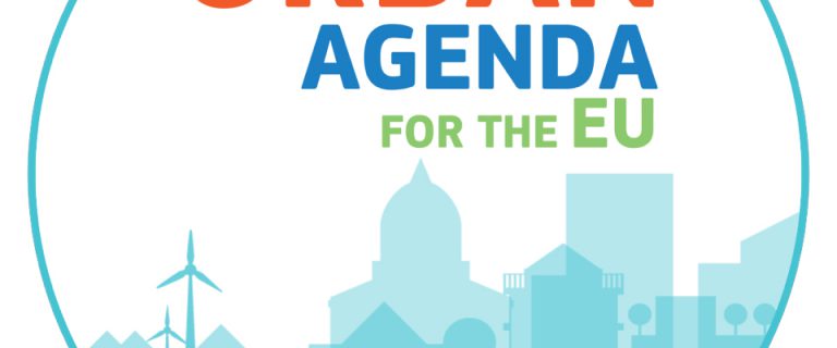 Het logo van de Europese Agenda Stad, ofwel de Urban Agenda for the EU. Het betreft een cirkelvormige afbeelding met daarin een gestileerde, getekende skyline van een stad, met huizen, windmolens, torens en religieuze gebouwen. Boven de skyline staat de tekst 'Urban agenda for the EU'.